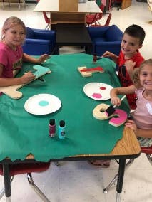Three children painting wooden shapes at a table