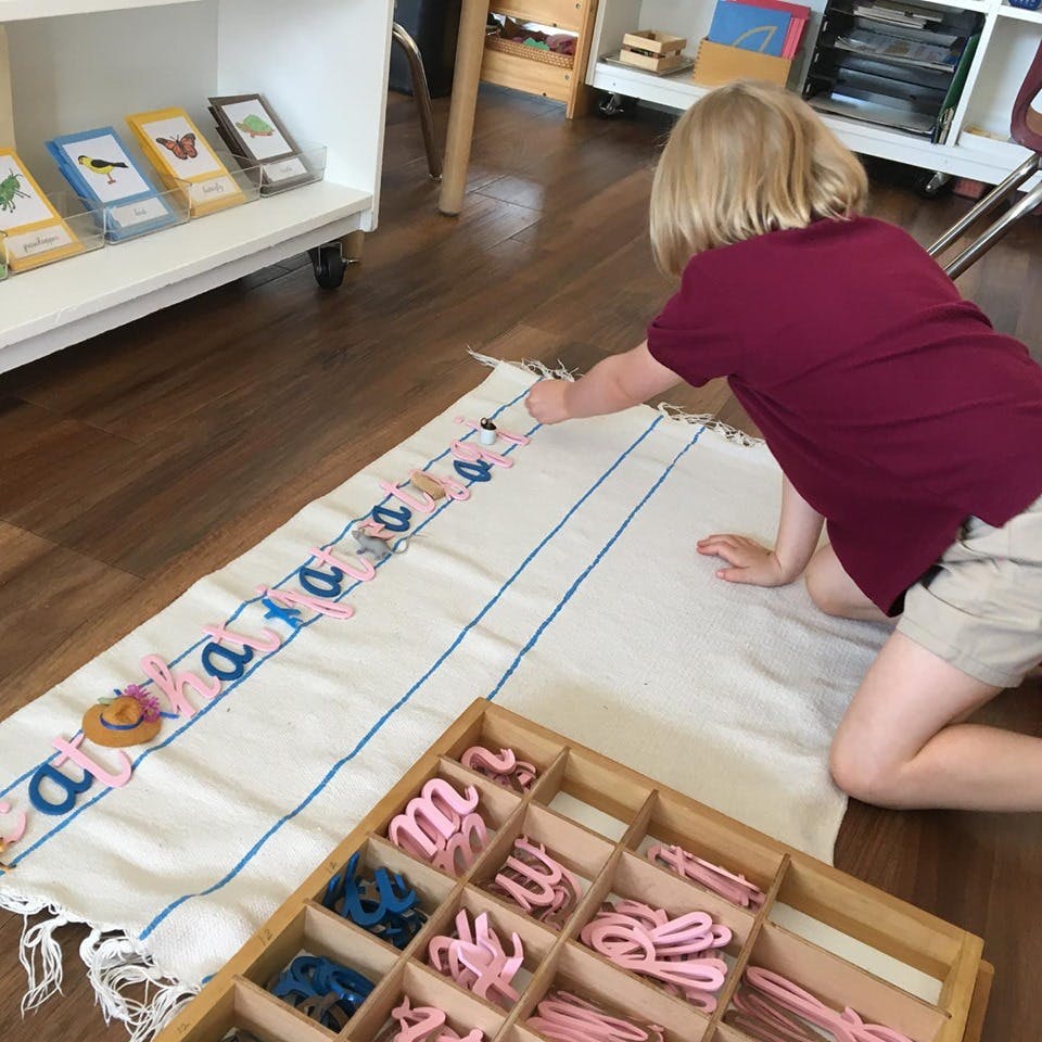 Child kneeling on a rug, arranging letter cutouts