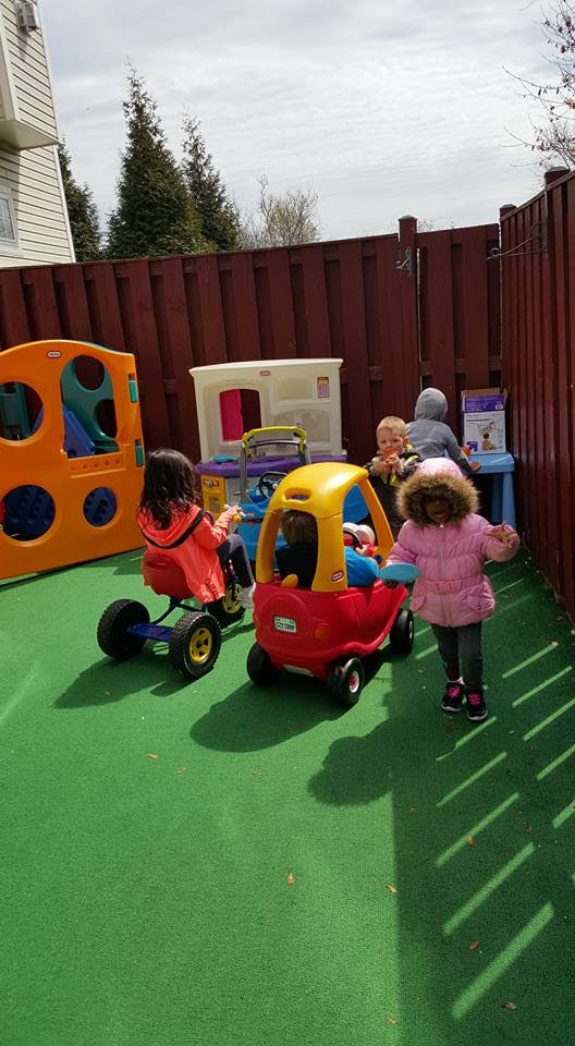 Children playing with ride-on toys in a fenced outdoor area
