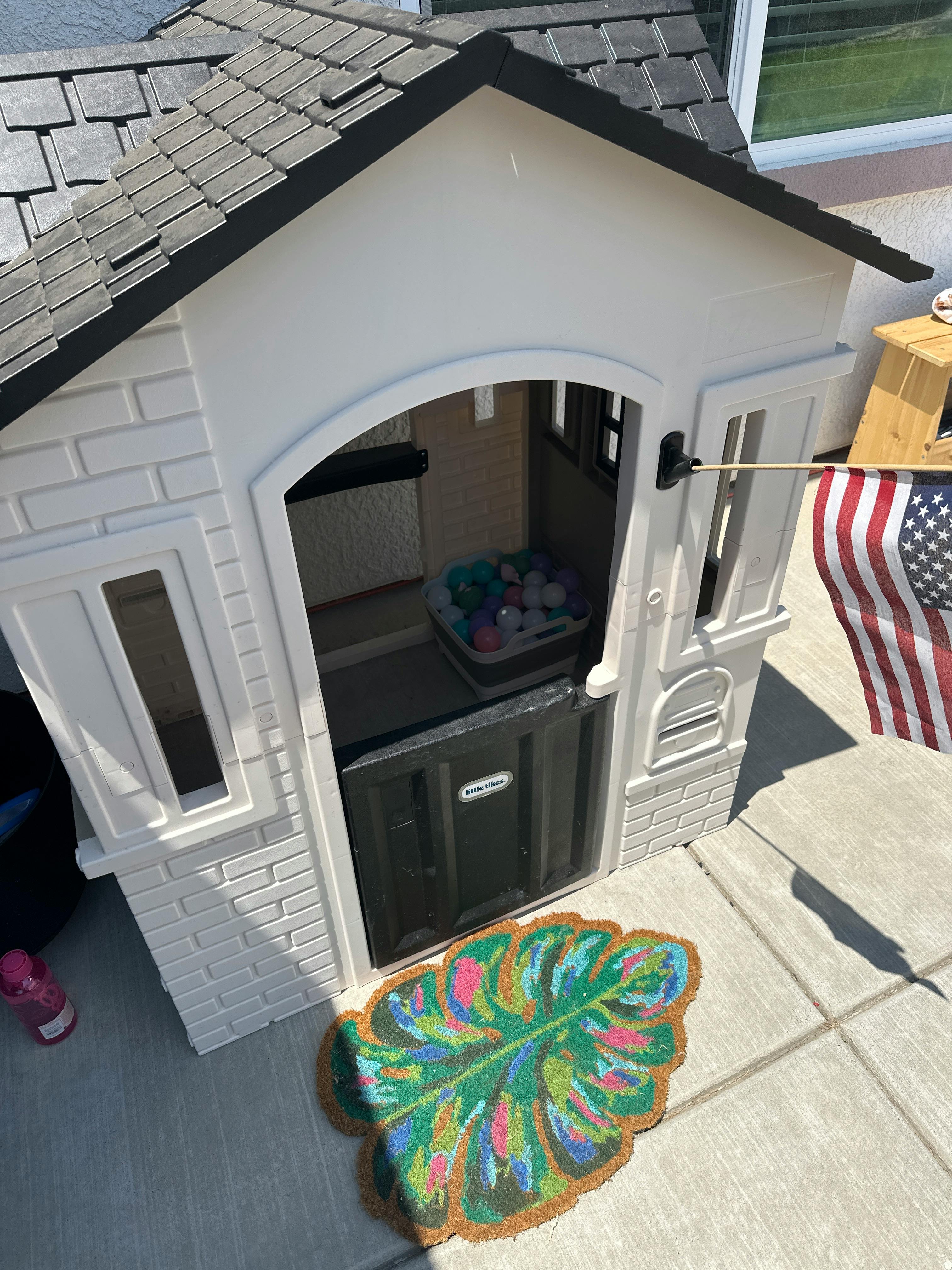 White playhouse with a green leaf-shaped mat in front