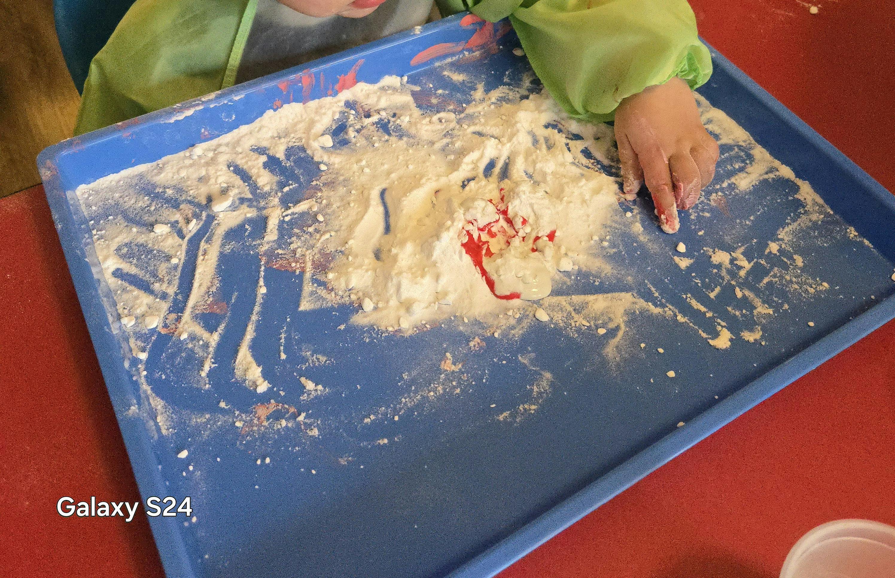 Child's hand playing in flour and red liquid on a blue tray