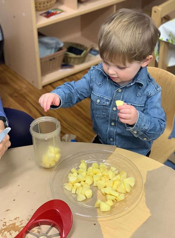 Child holding a piece of apple, with diced apples on a plate and in a container