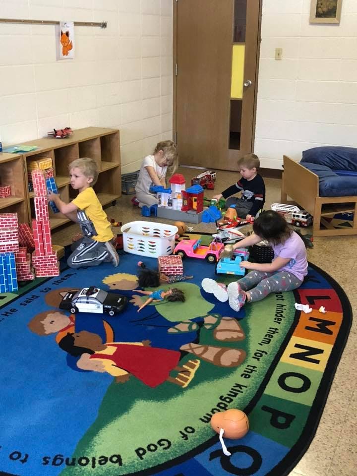 Children playing with toys on a colorful rug in a classroom