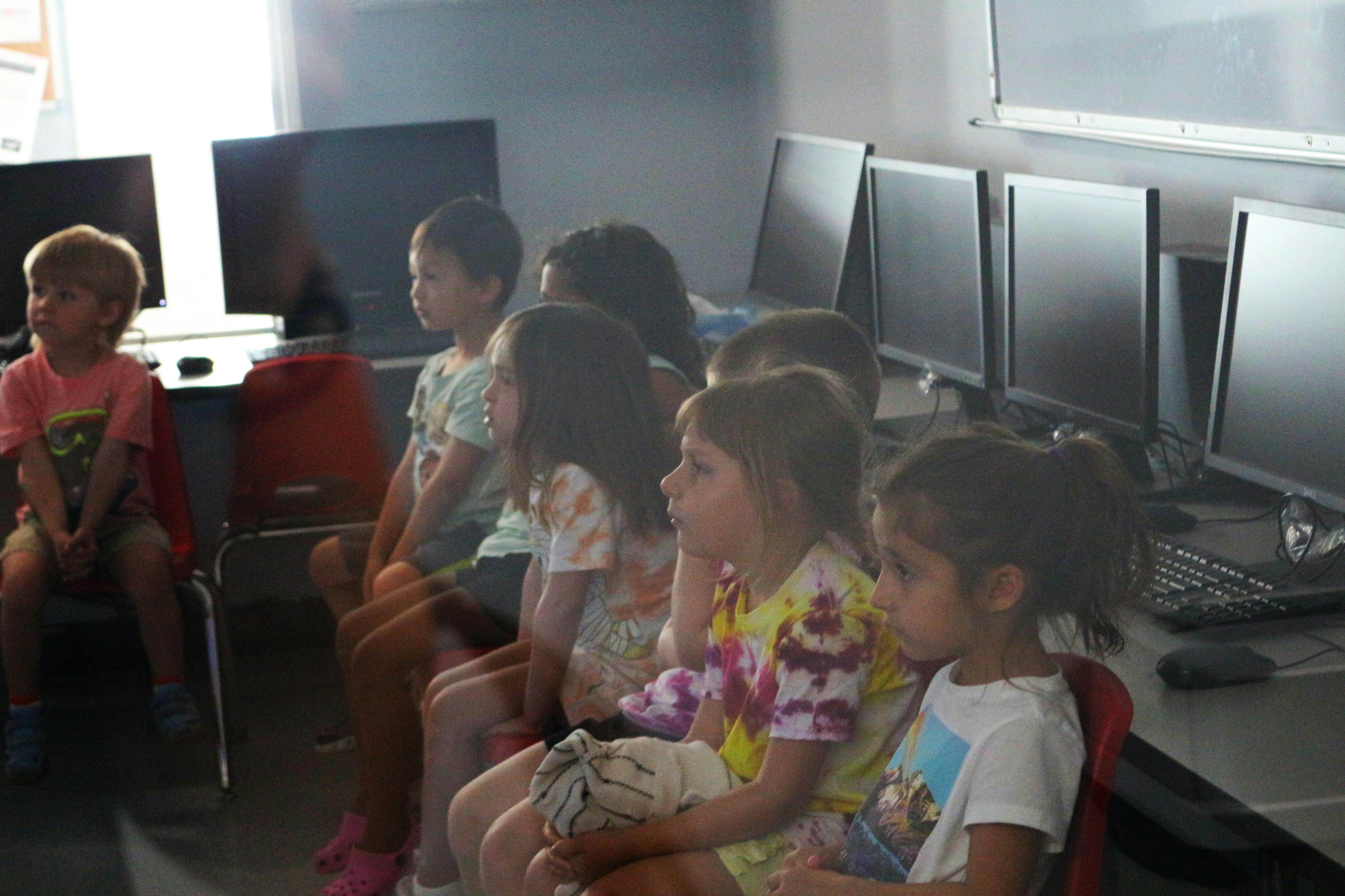 Children sitting in a row in front of computer monitors