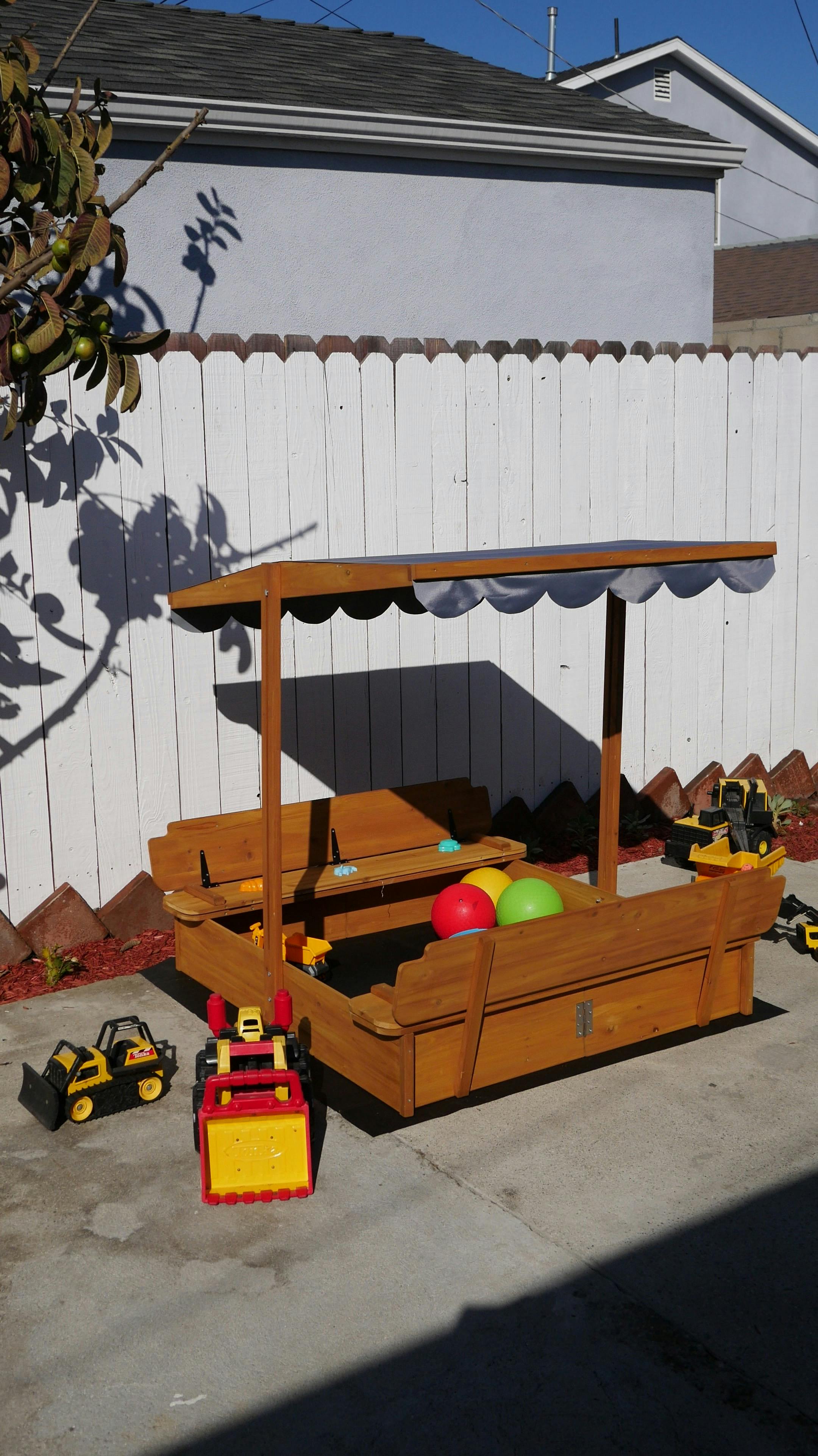 Wooden sandbox with a canopy and toy construction vehicles