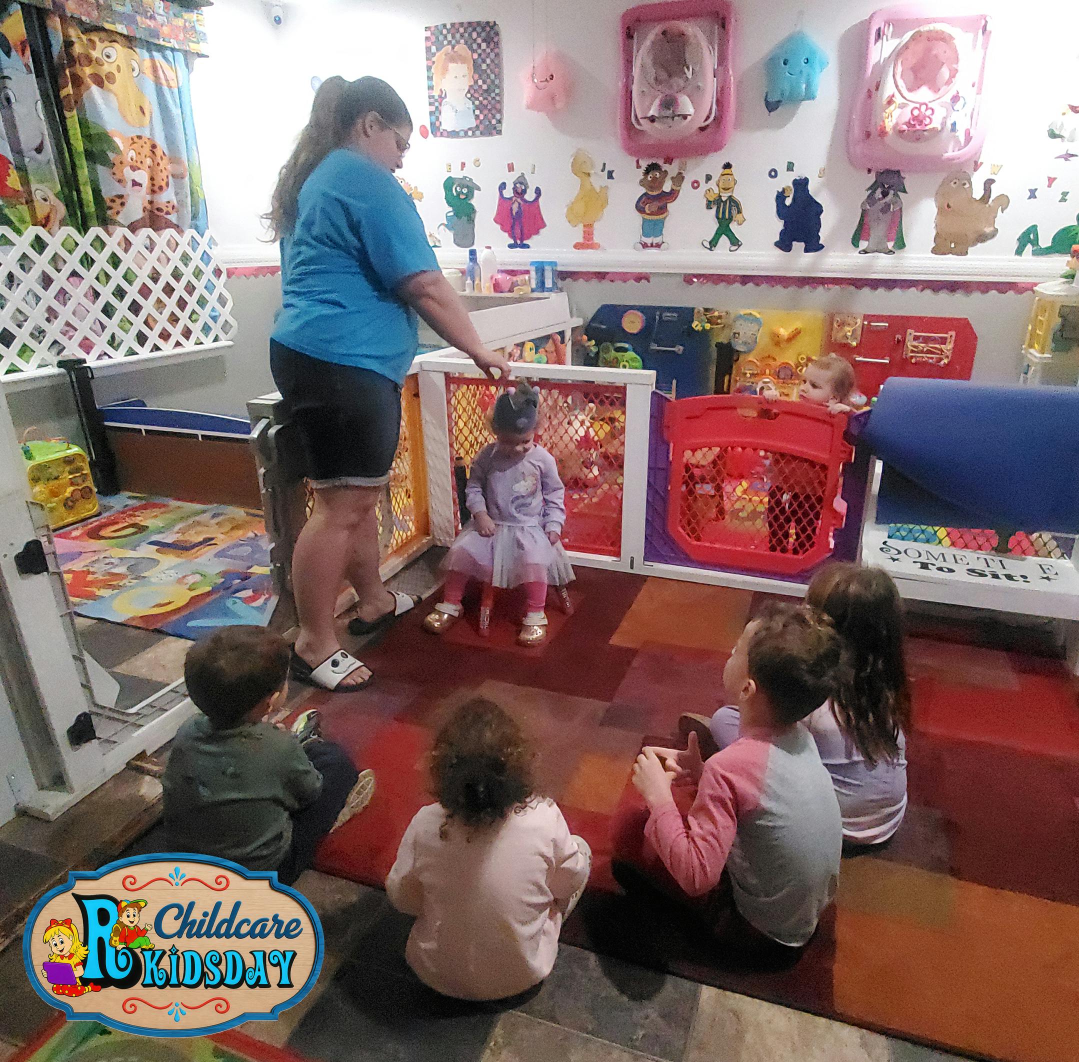 Adult assisting a child in a chair while other children sit on the floor