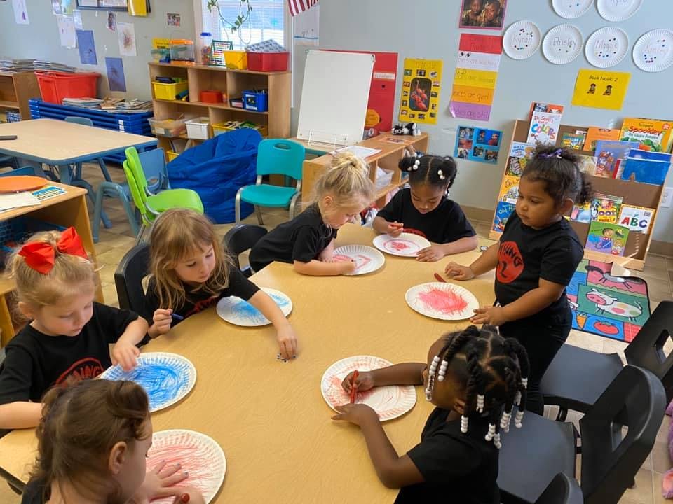 Children sitting at a table painting paper plates in a classroom