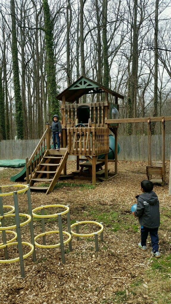 Two children on a playground with a wooden playset and swing