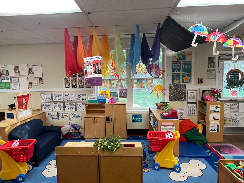 A colorful classroom with play areas, decorated with scarves and paper umbrellas