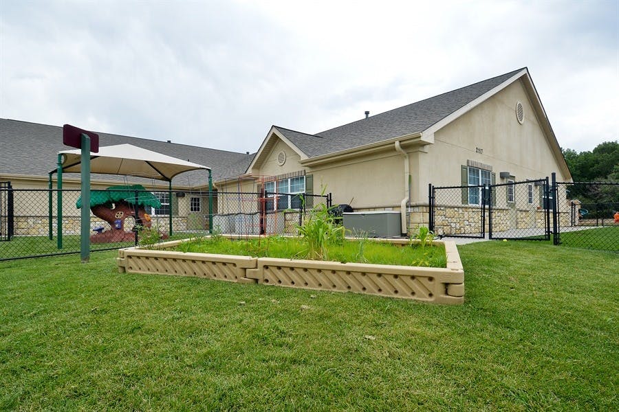 Building exterior with a fenced yard, playground, and raised garden bed