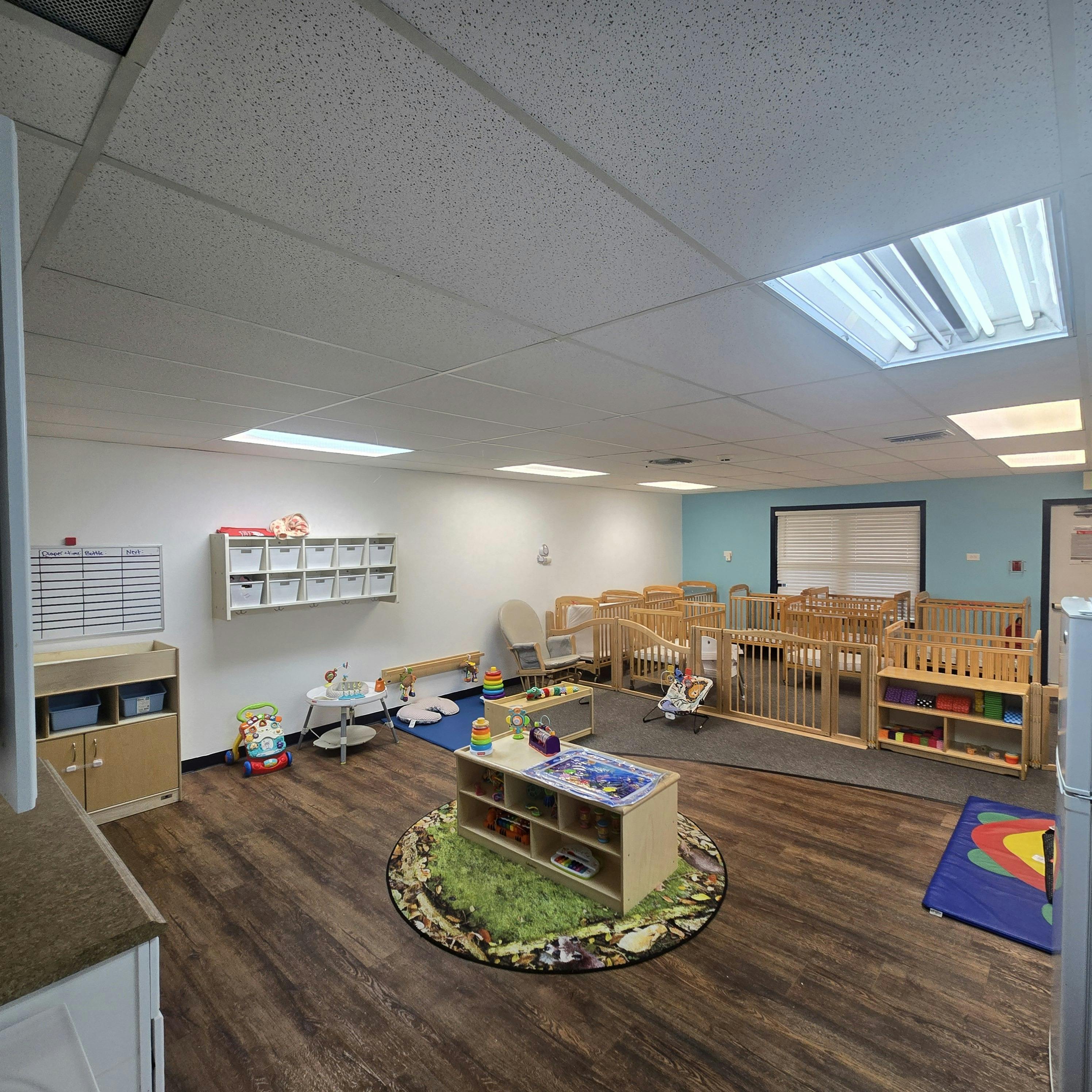 A daycare room with cribs, play mats, shelves with toys, and a changing table