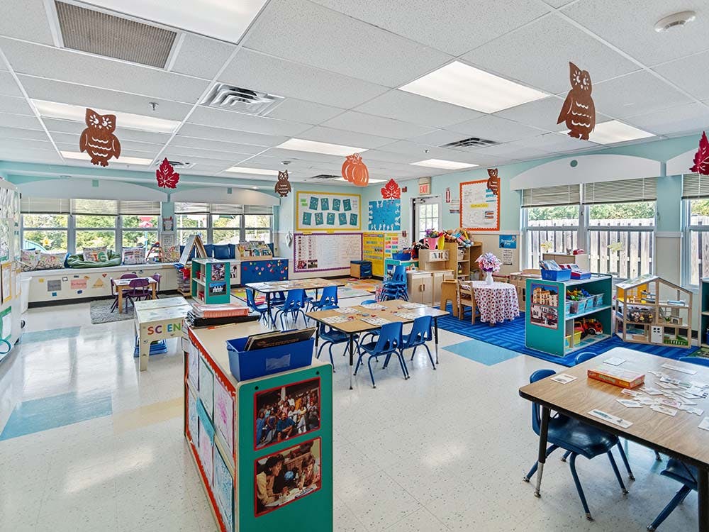 An empty preschool classroom with small tables, chairs, and colorful decorations