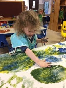 Child finger painting on a large sheet of paper in a classroom
