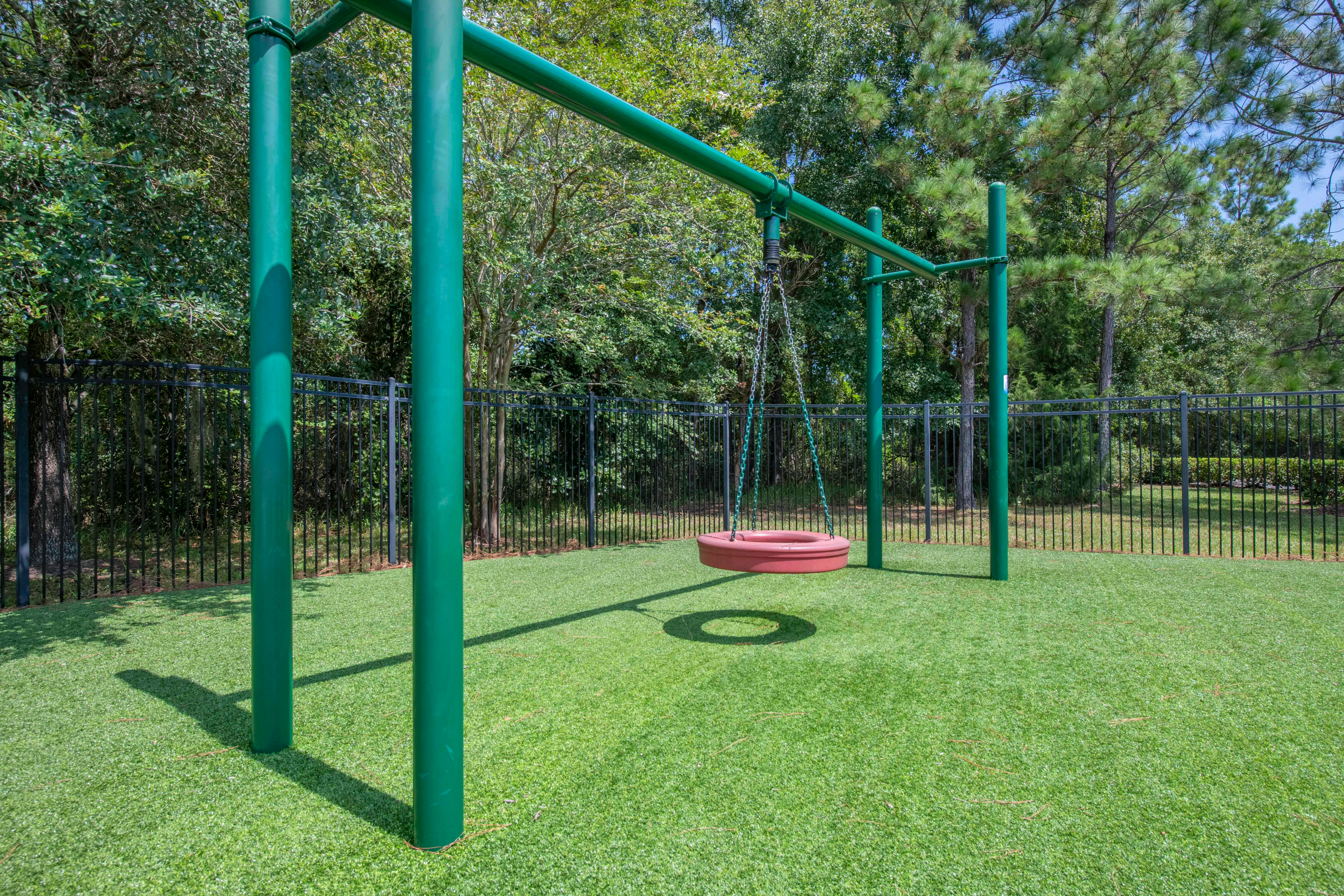 A green swing set with a single red tire swing over artificial green turf