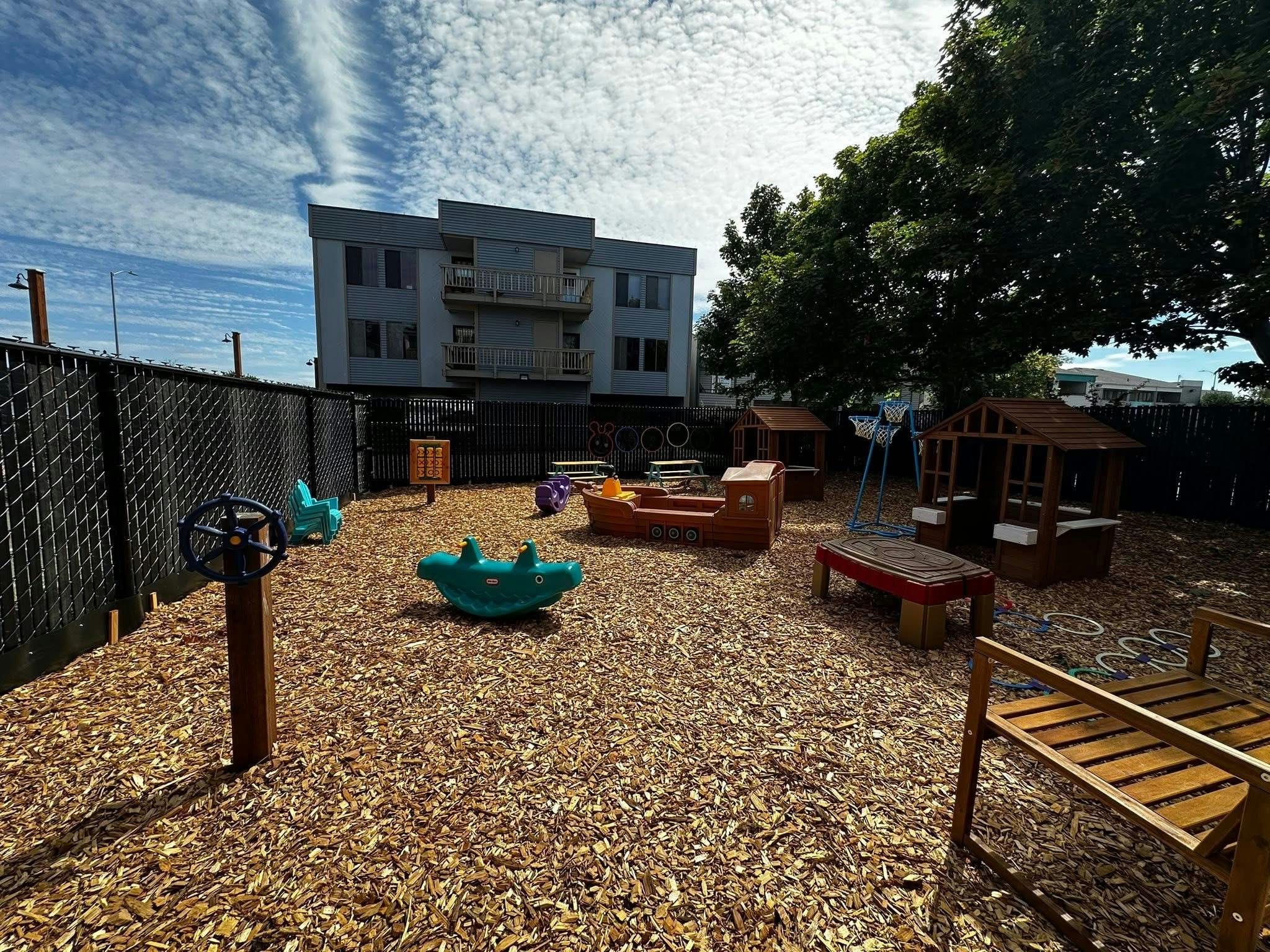 Outdoor playground with wood chips, play structures, and a building in the background