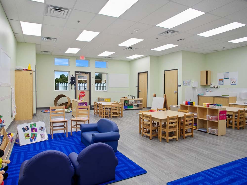 Empty classroom with small tables and chairs, and blue rugs on the floor