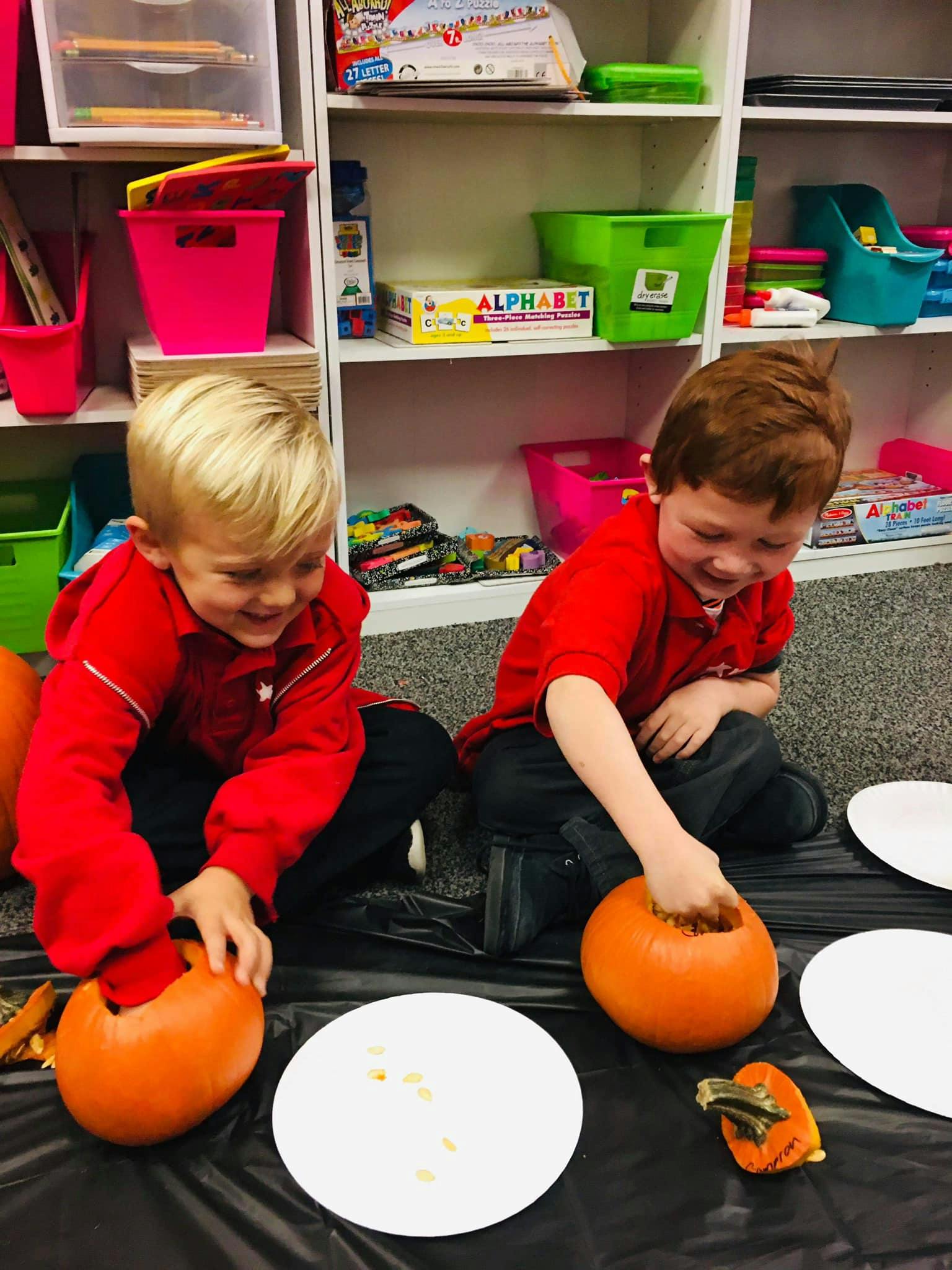 Two children carving pumpkins in a classroom