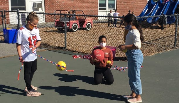 Three children playing with a jump rope and balls outdoors