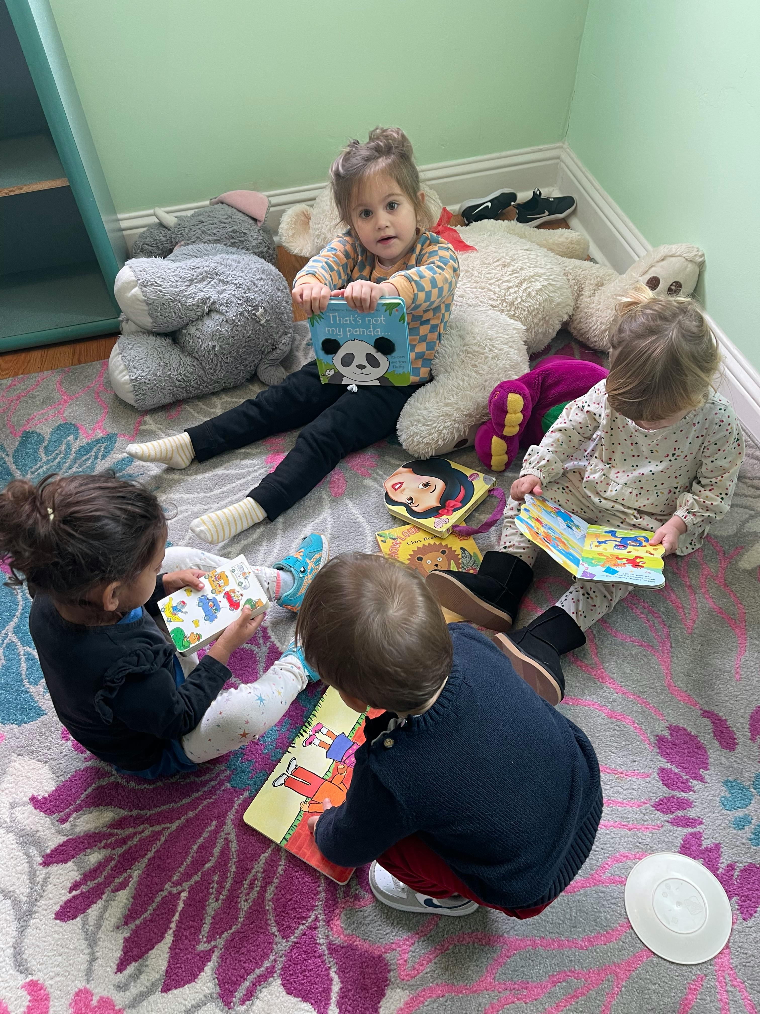 Four children sitting on a rug with books