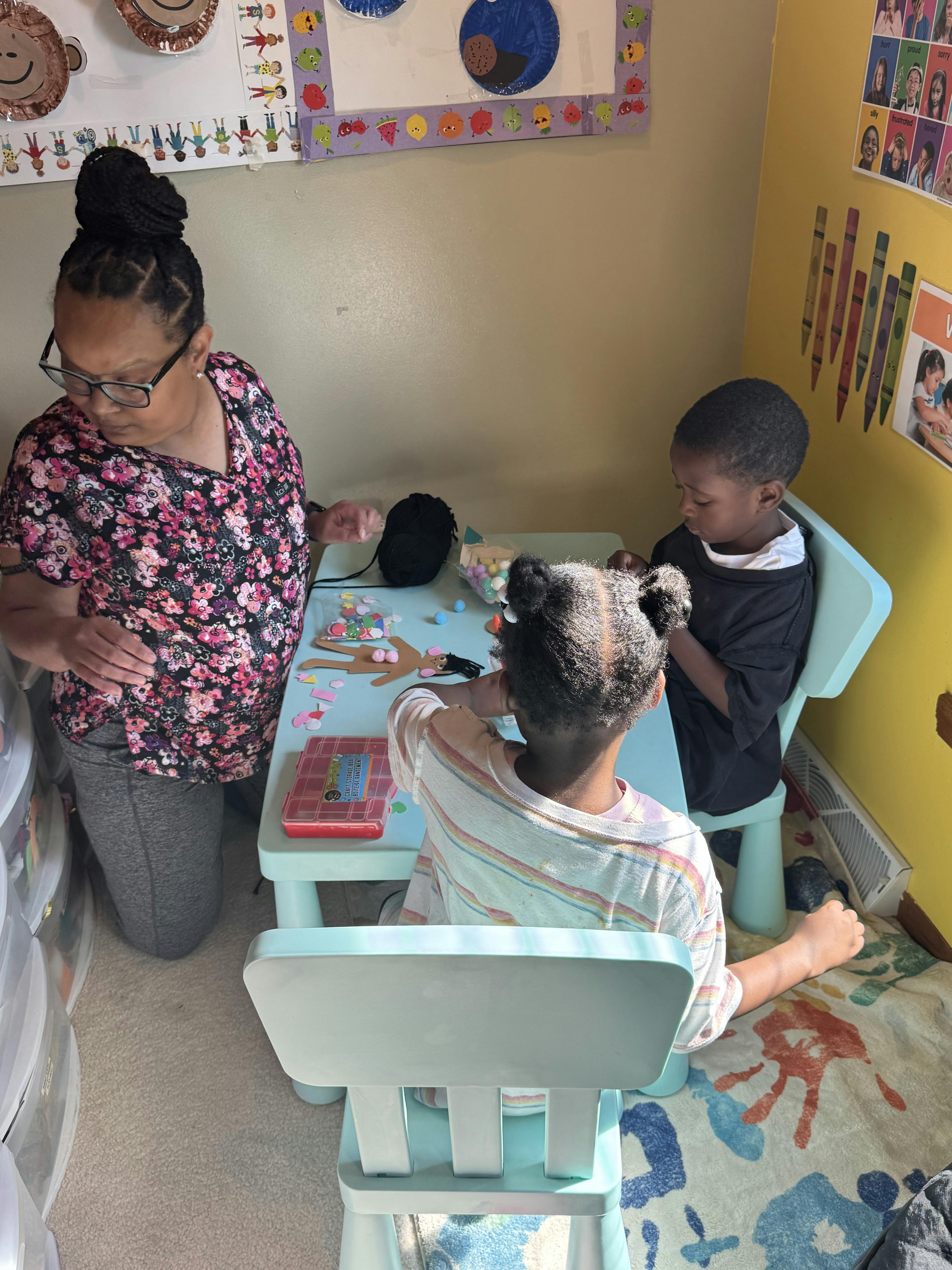 Adult assisting two children with a craft project at a table