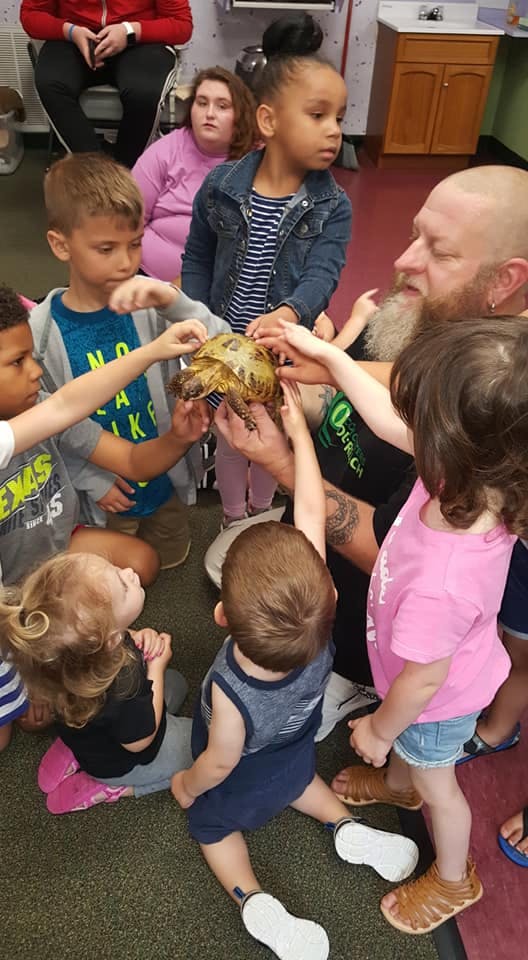 Adult holding a turtle while children reach out to touch it