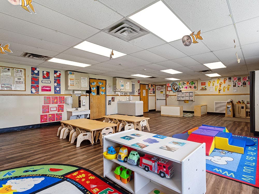 Children's classroom with small tables and chairs, shelves, play mats, and cubbies