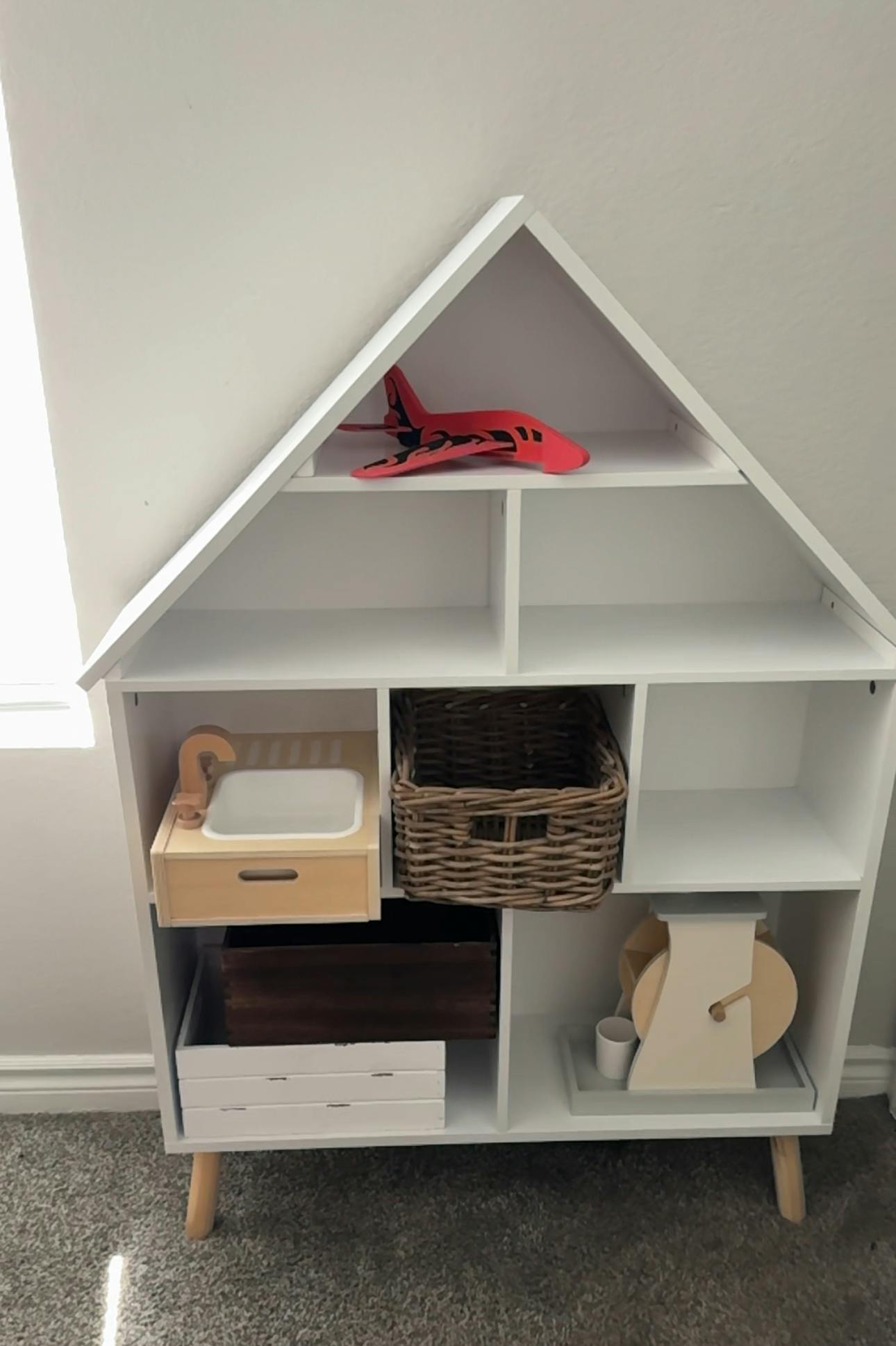 White house-shaped shelf with various items including a red toy airplane
