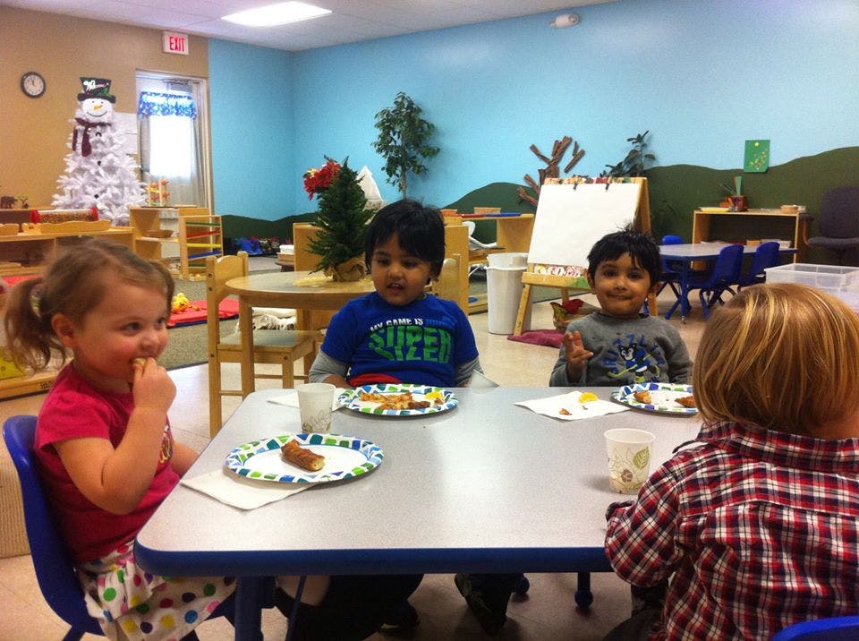 Four children sitting at a table with plates in a classroom