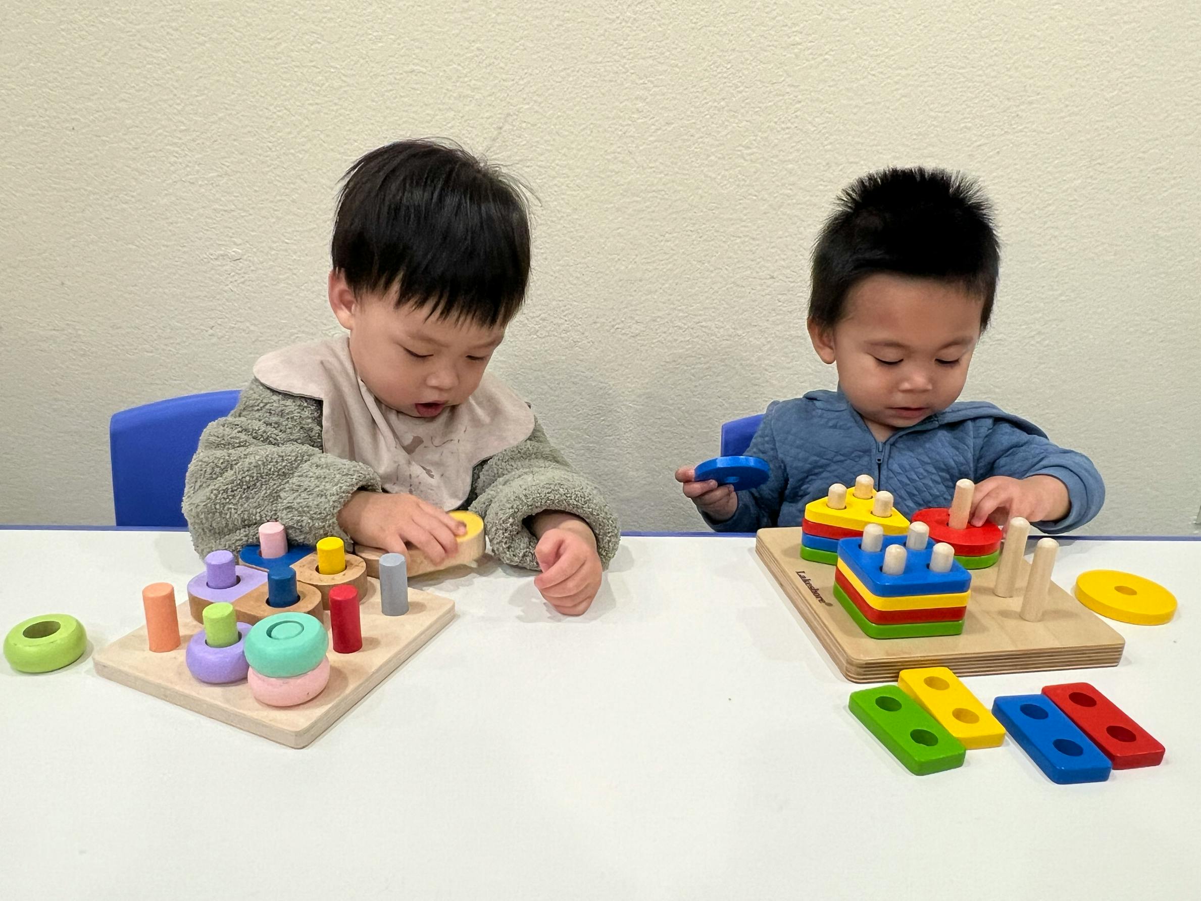 Two children playing with wooden stacking toys at a table