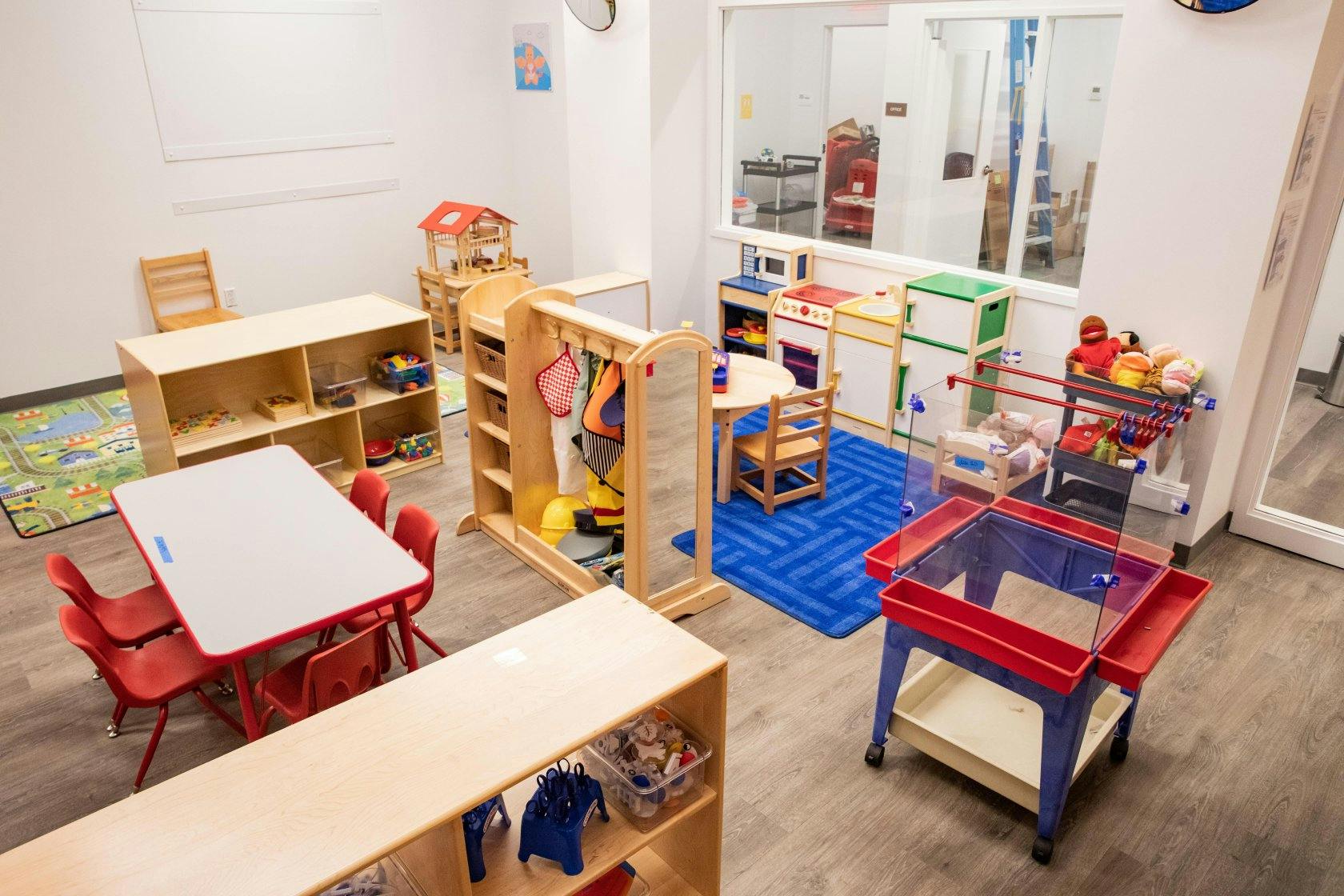 Classroom with play kitchen, tables and chairs, and play mats