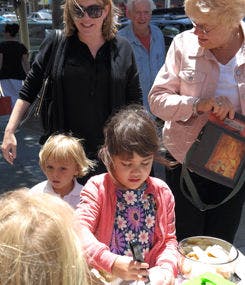 Child drawing at a table with adults and another child nearby