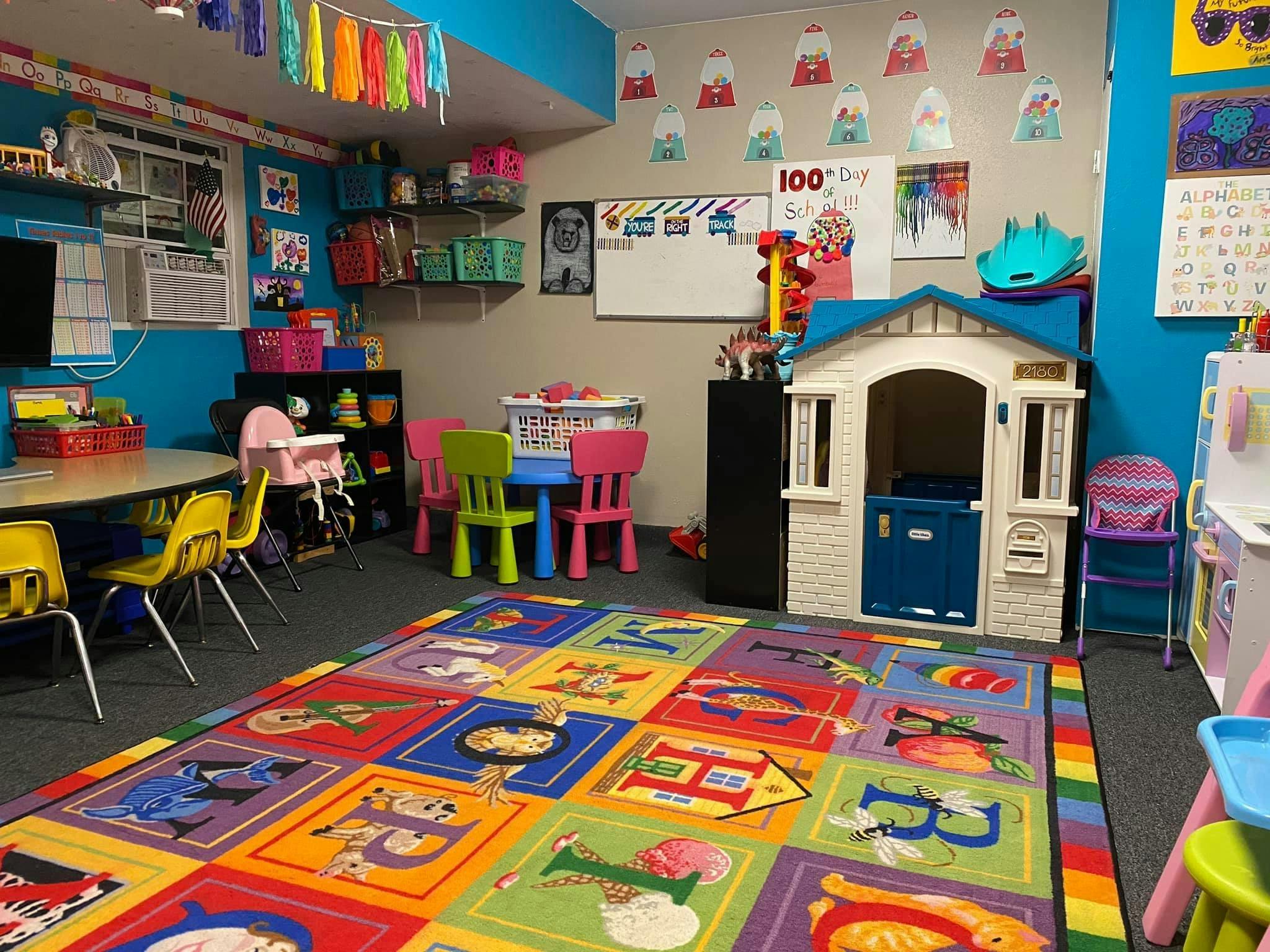 Playroom with colorful rug, small tables and chairs, and a playhouse