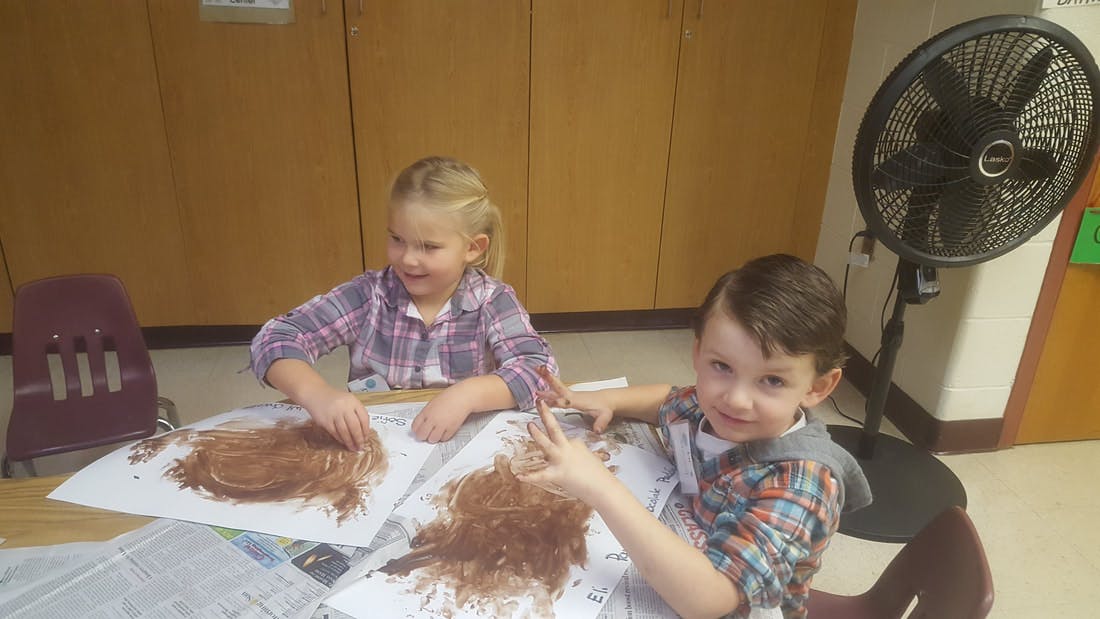 Two children doing an art project with brown material