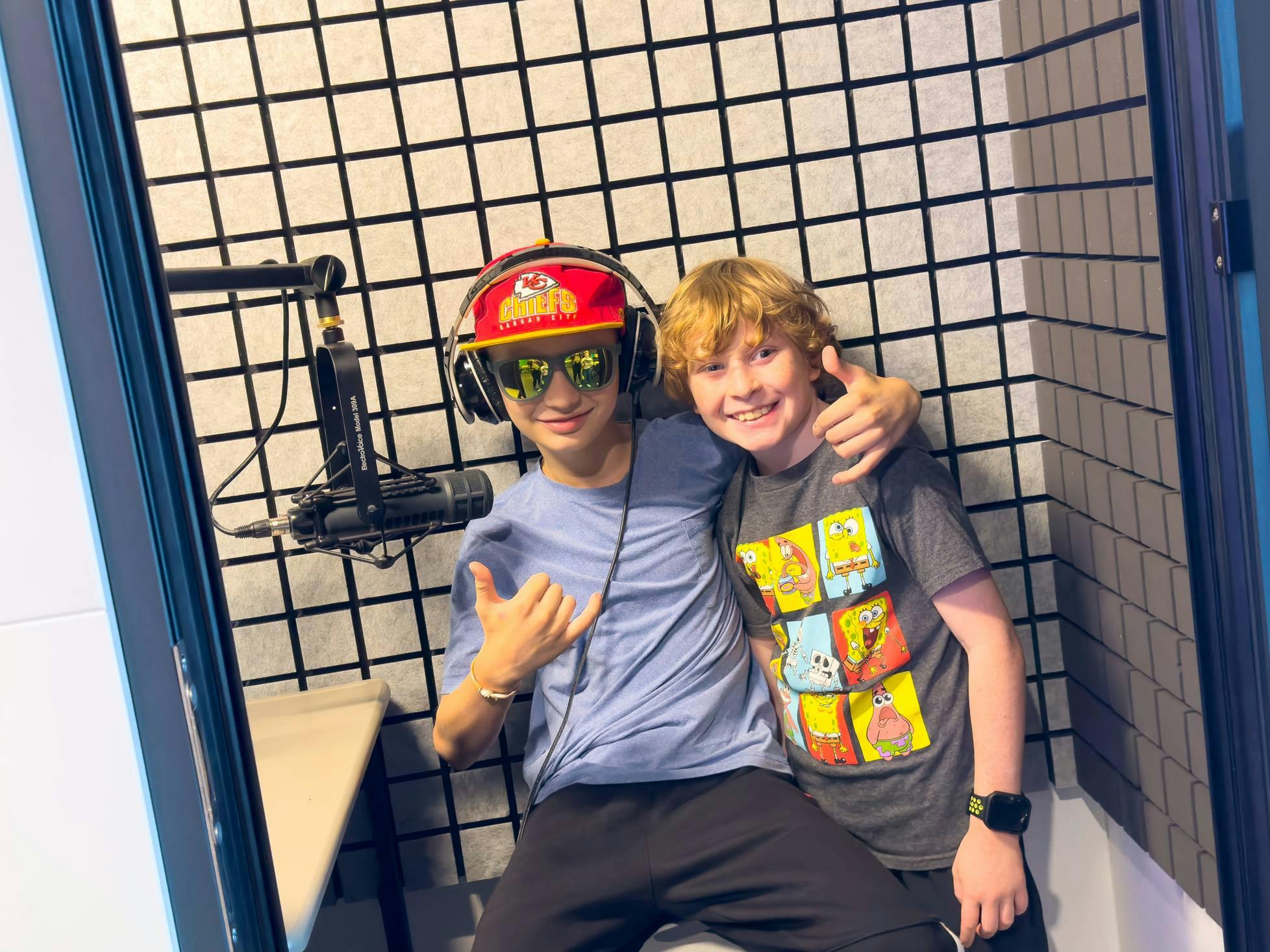 Two children posing in a recording booth, one wearing headphones and sunglasses