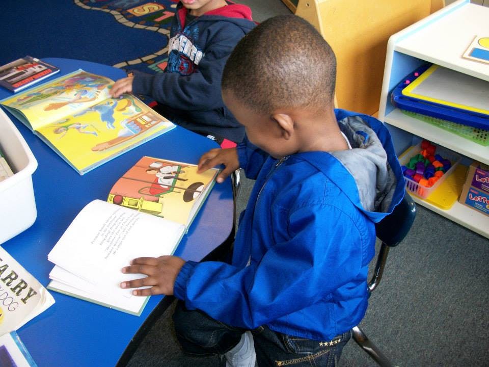 Child in blue jacket reading a book at a table