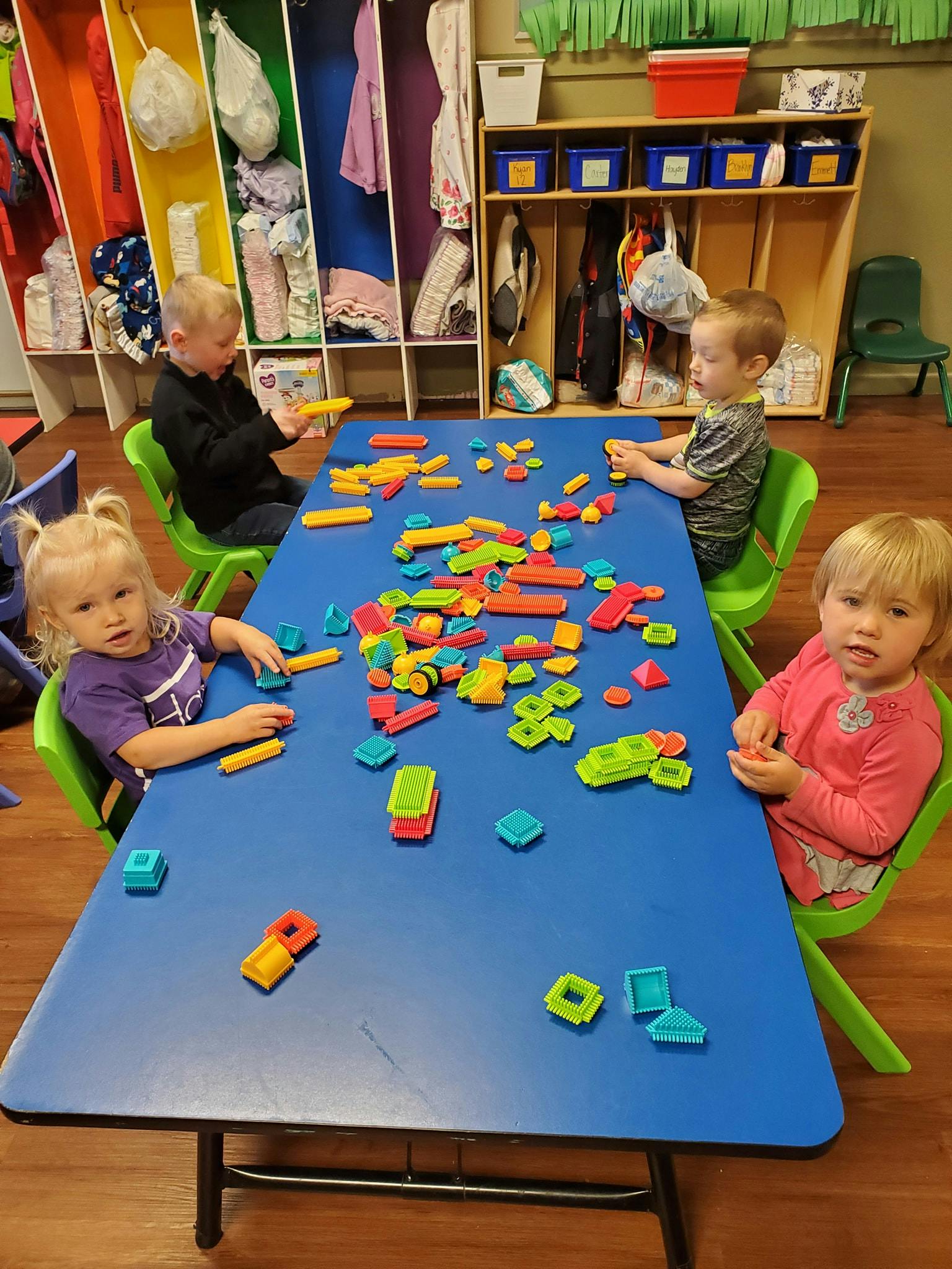 Four children playing with colorful building blocks at a blue table