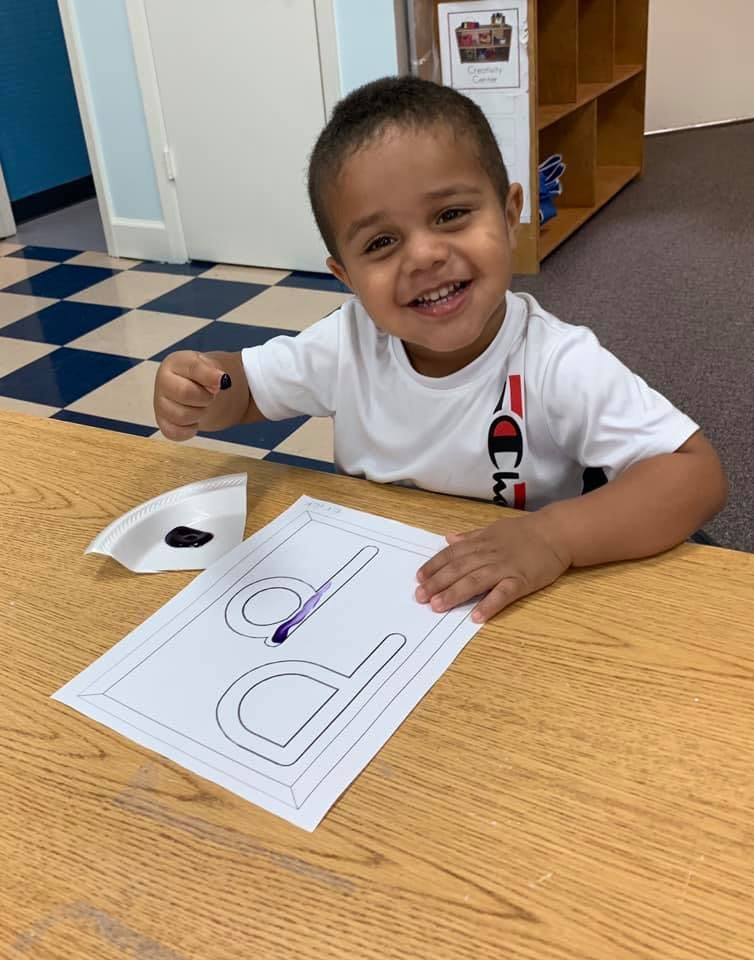 Child painting a letter on paper at a table