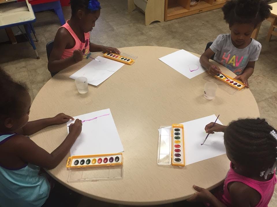 Four children painting at a round table in a classroom