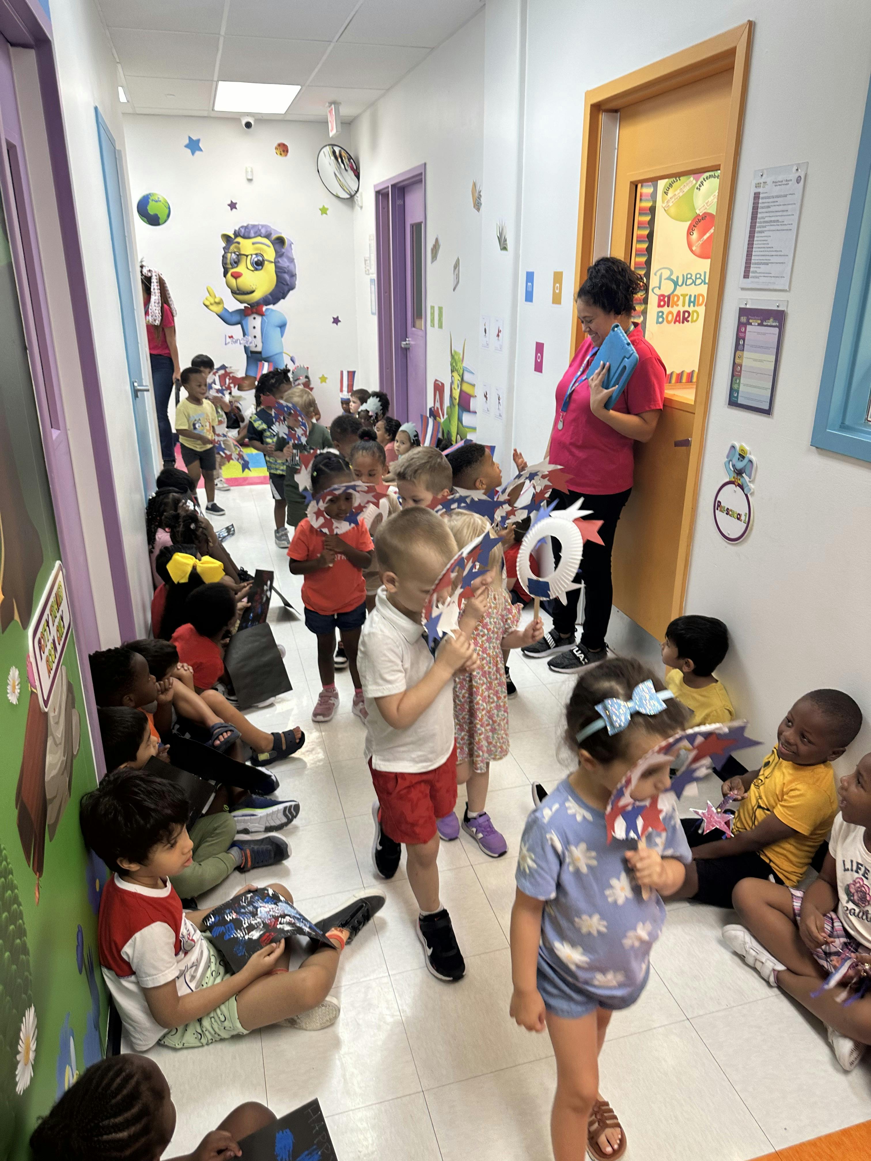 Children sitting and standing in a colorful hallway with a teacher