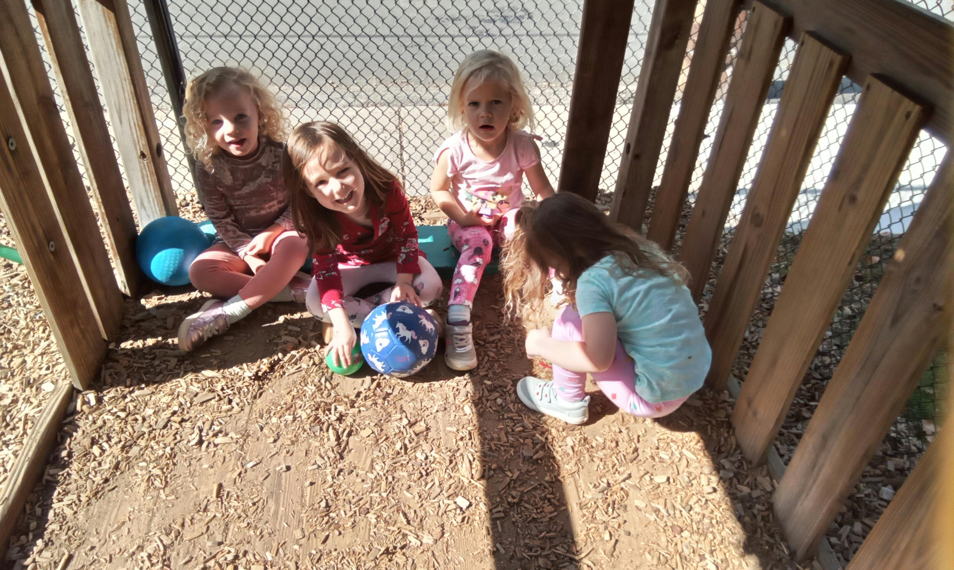 Four children playing with balls in a wooden structure