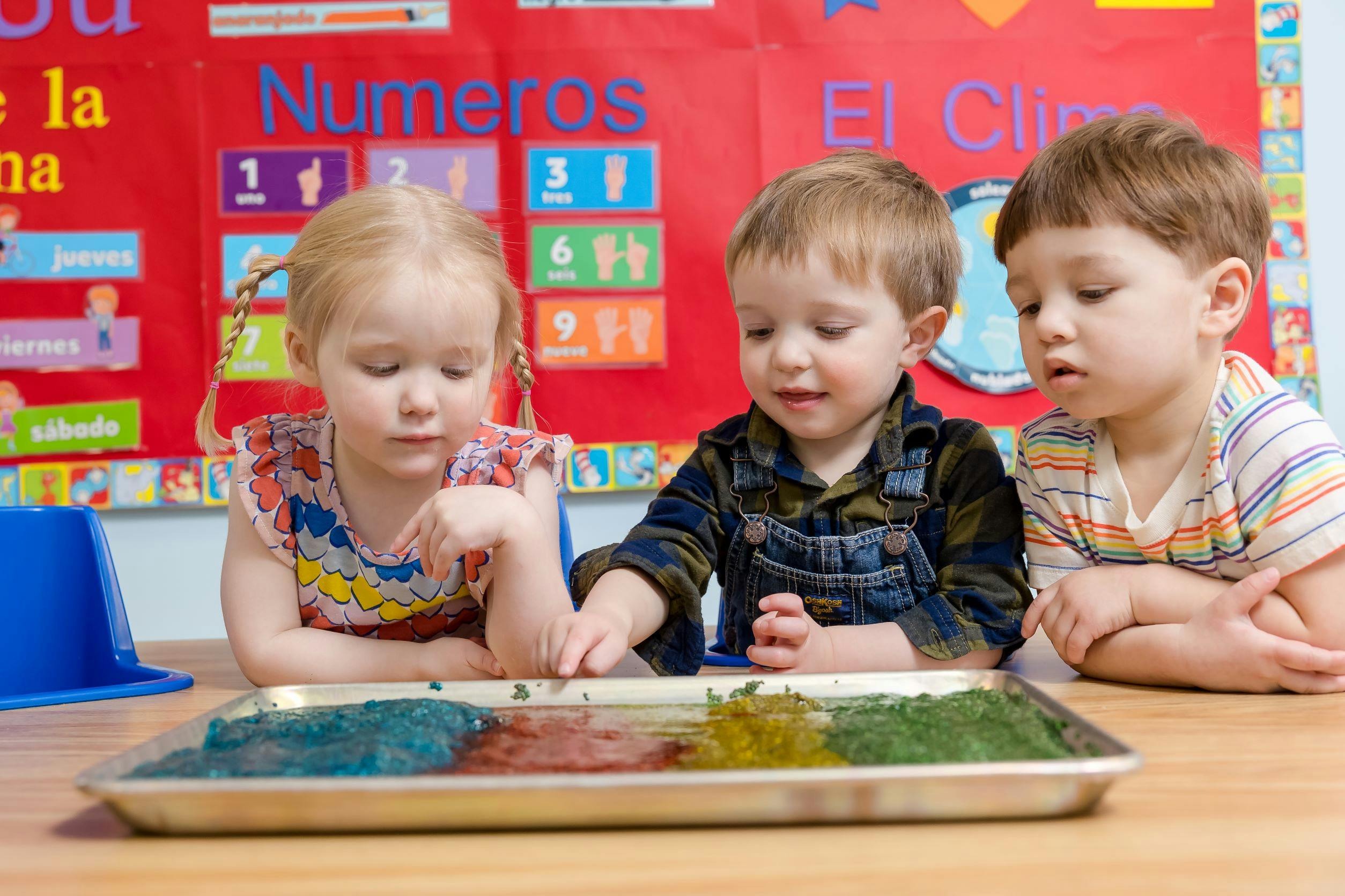 Three children playing with colorful sensory materials in a tray