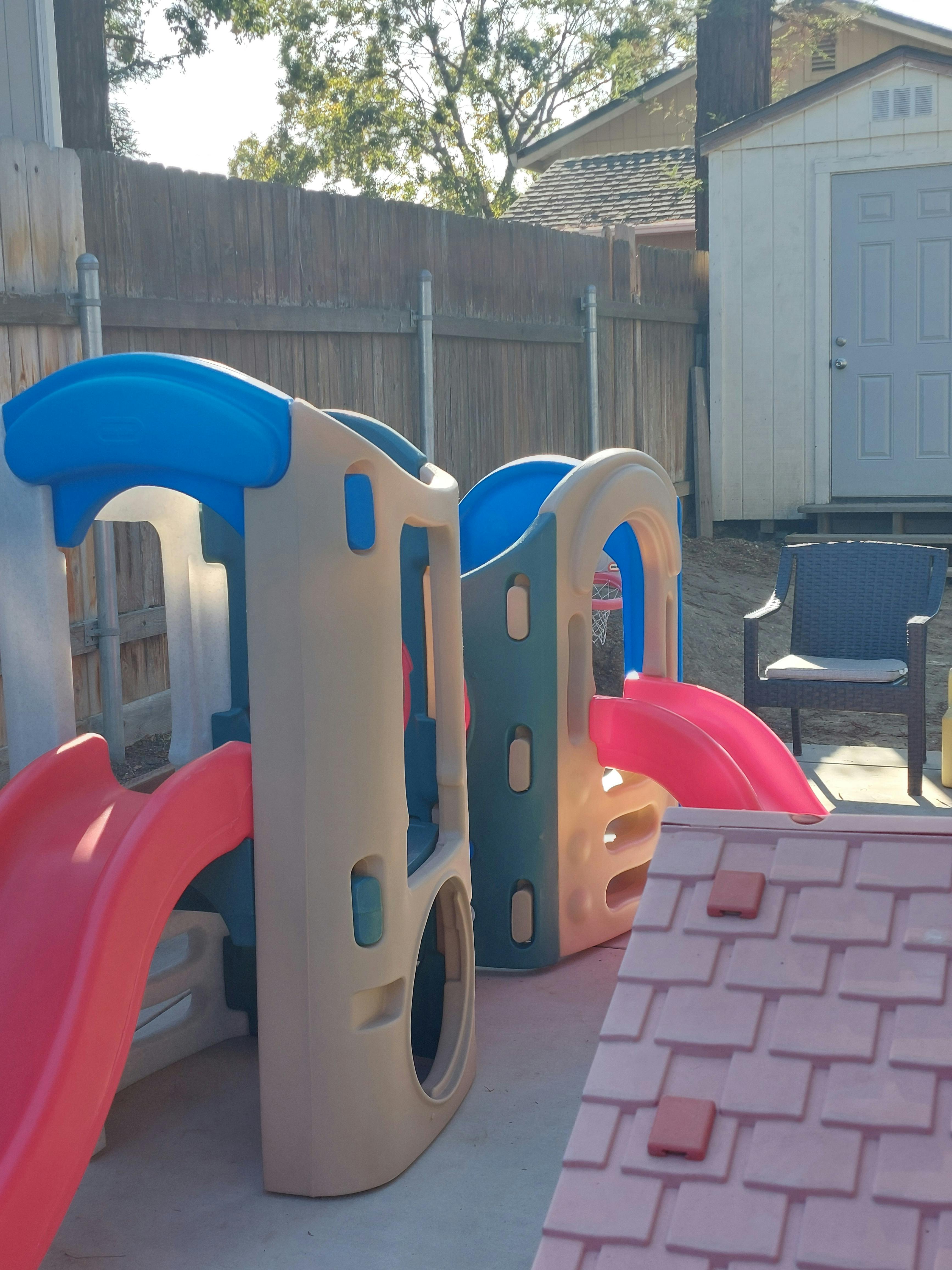 Two plastic play structures with slides in a backyard