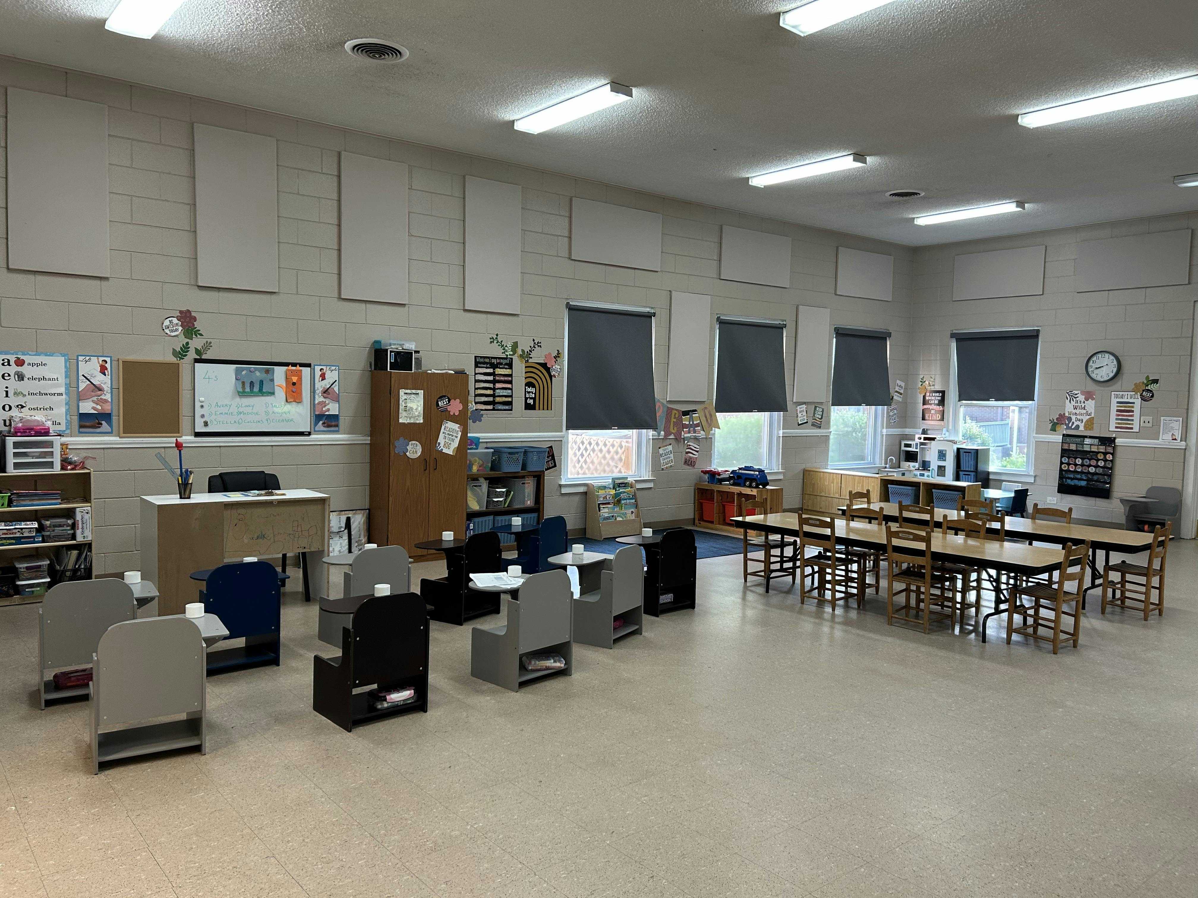 Empty classroom with small desks and chairs, a whiteboard, and windows