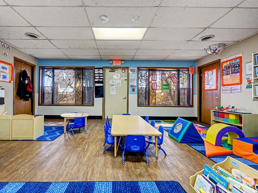Classroom with small tables and chairs, soft play equipment, and windows