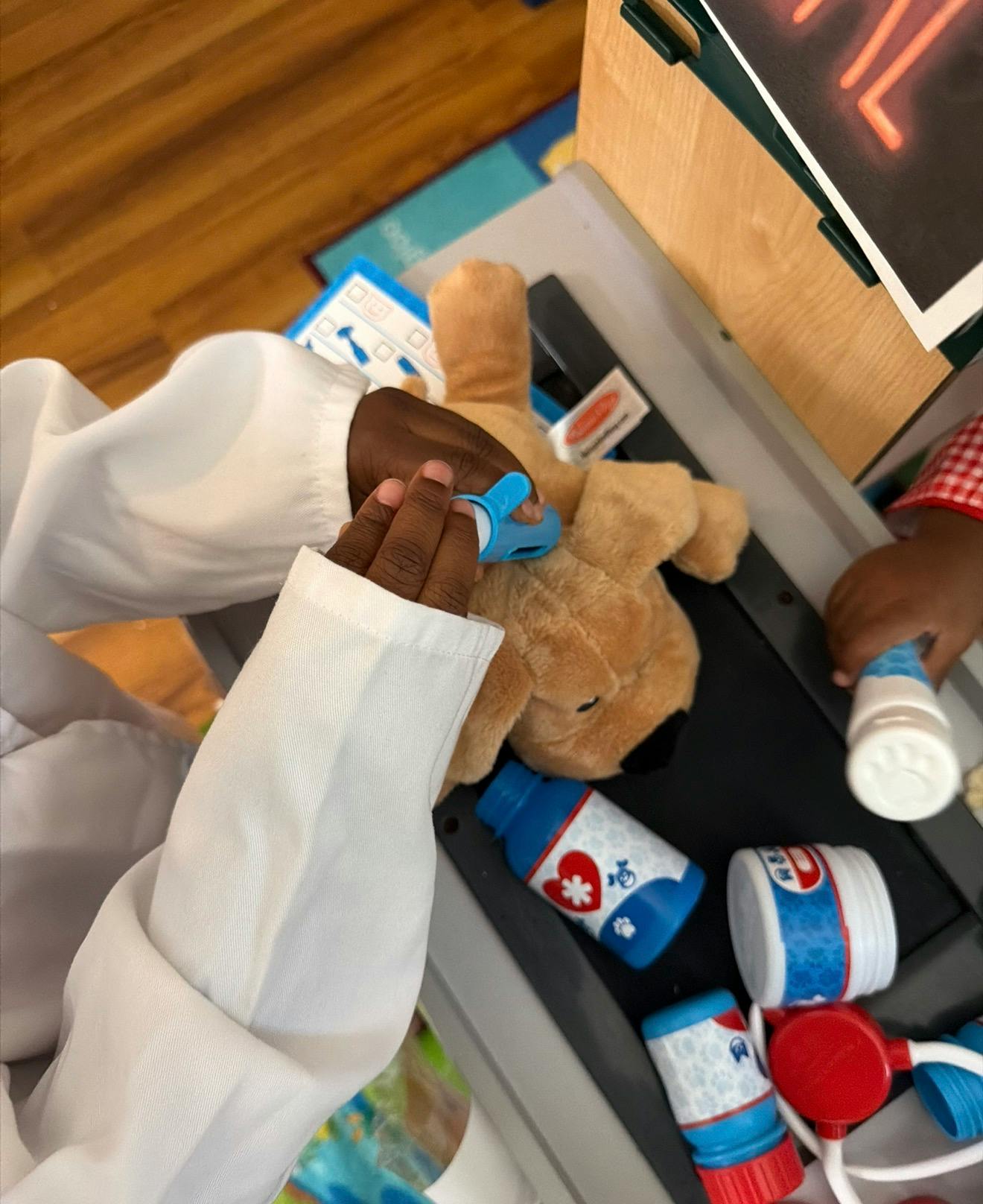 Child in a white coat playing with a stuffed dog and toy medical equipment