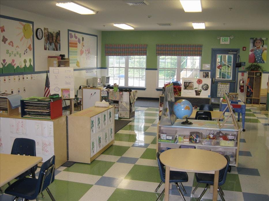 An empty classroom with bright lighting, tables and chairs, and learning materials