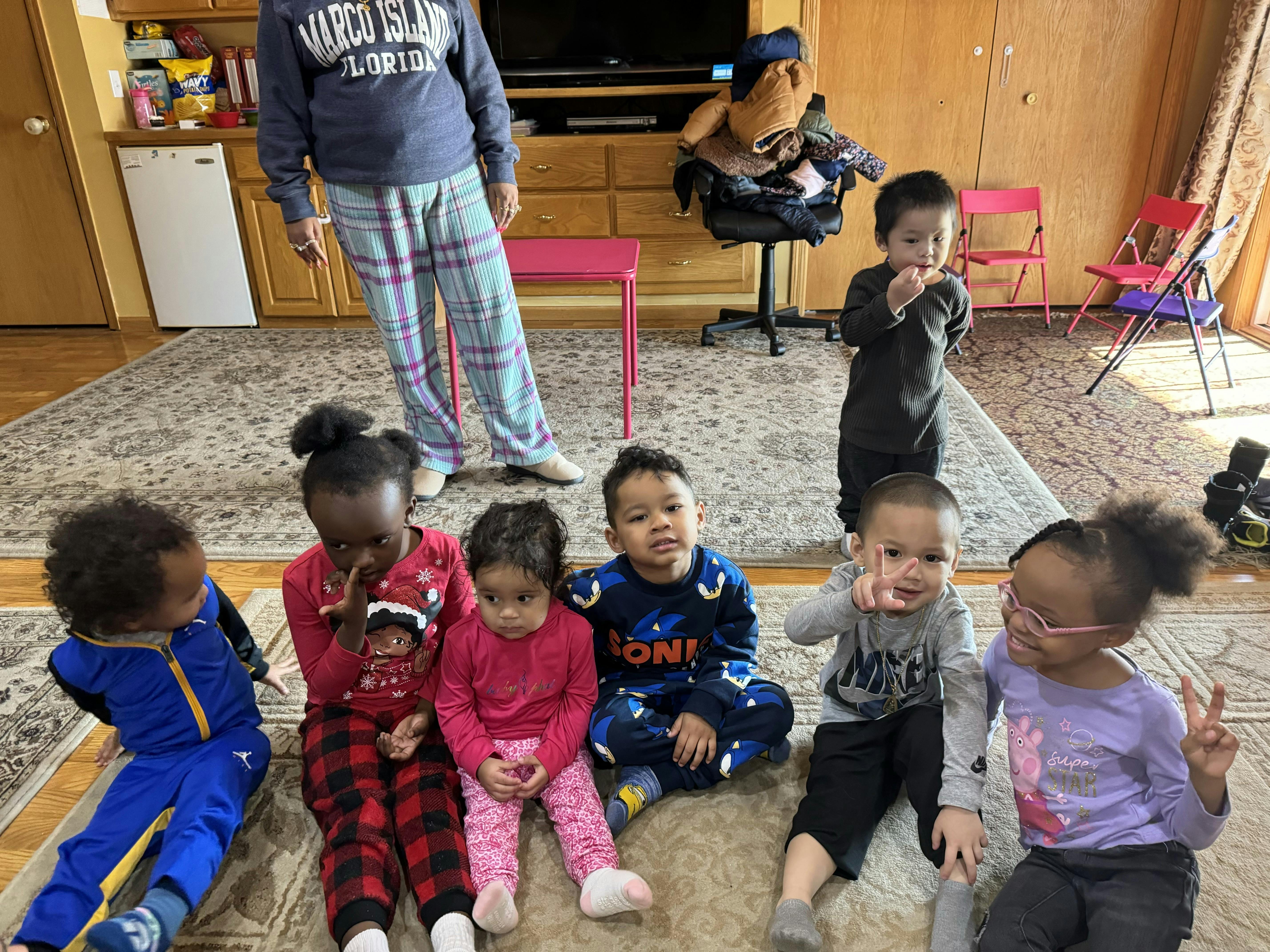 Person standing behind several children sitting on a rug
