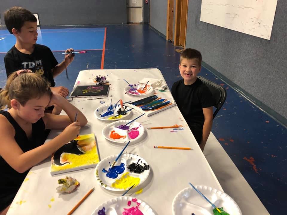 Three children painting at a table with paint palettes