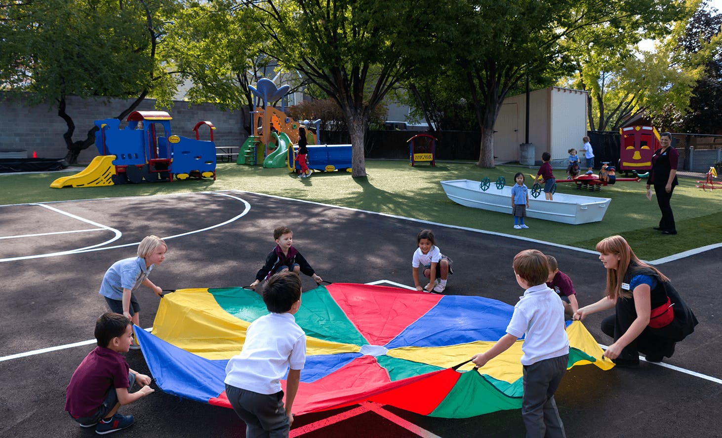 Children and an adult playing with a colorful parachute on a playground