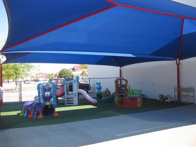Outdoor playground with play structures under a blue shade canopy